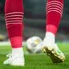 a close up of a soccer player's feet with a ball in the background