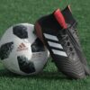 black adidas cleats lean on white and black adidas soccer ball on green grass