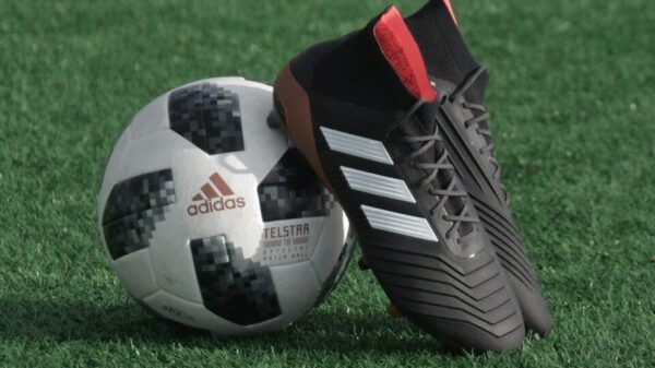 black adidas cleats lean on white and black adidas soccer ball on green grass