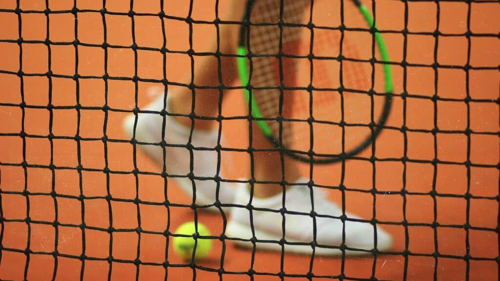 person wearing pair of white low-top sneakers while holding Wilson tennis racket