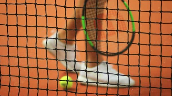 person wearing pair of white low-top sneakers while holding Wilson tennis racket