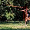 Two women practicing javelin throw outdoors in a lush forest setting in Colombia.