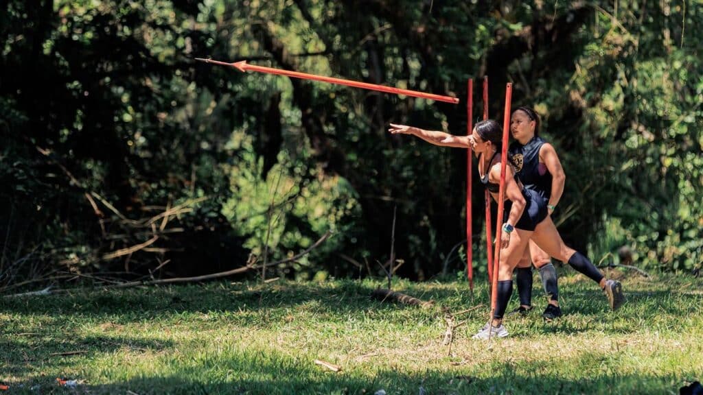 Two women practicing javelin throw outdoors in a lush forest setting in Colombia.