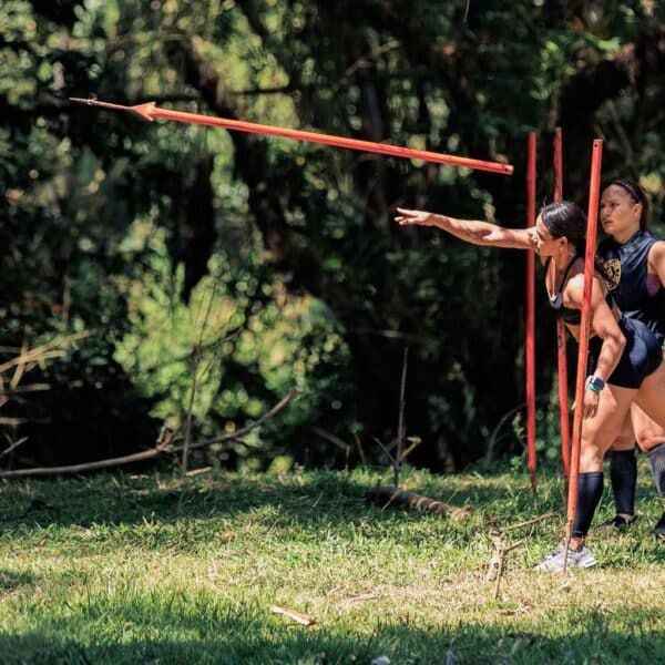 Two women practicing javelin throw outdoors in a lush forest setting in Colombia.