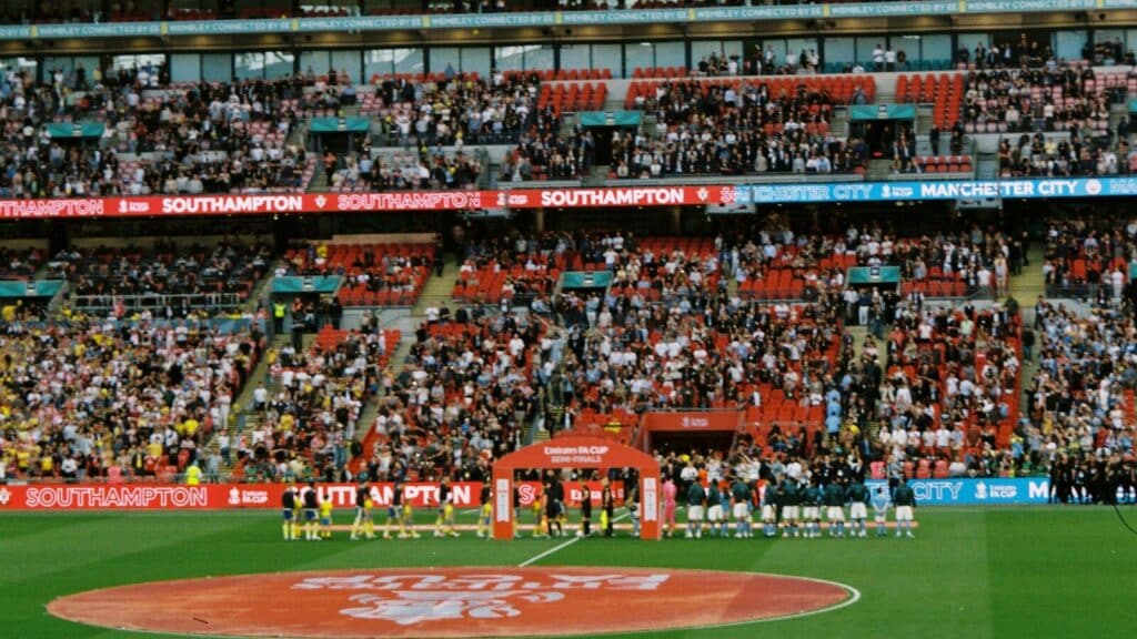 Crowd watches teams line up on a sports field.