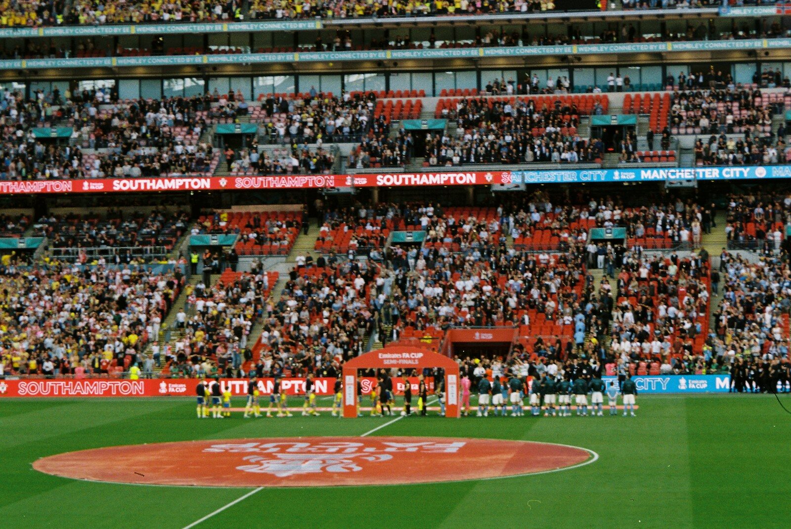 Crowd watches teams line up on a sports field.