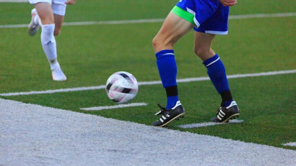 person in blue and white soccer jersey kicking soccer ball on field during daytime